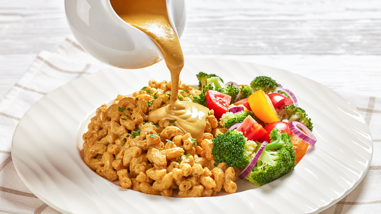 Nutritional yeast cheese sauce poured over mac and cheese with vegetables on plate