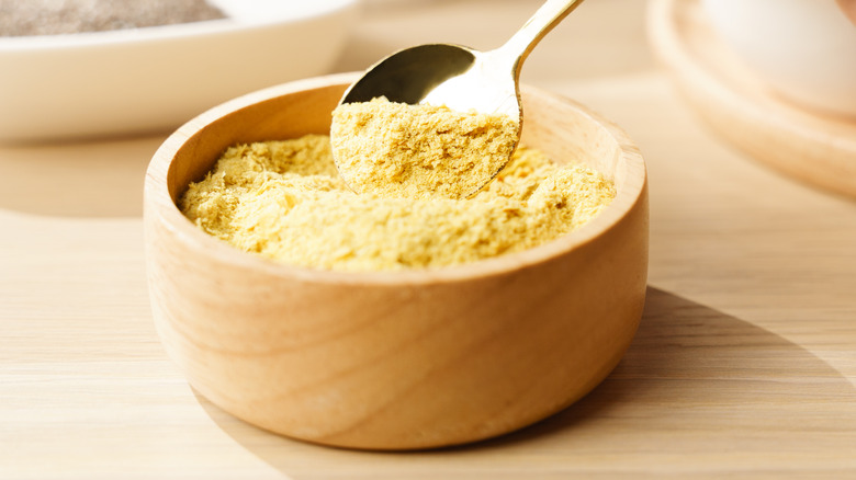 Nutritional yeast powder in wooden bowl scooped with spoon