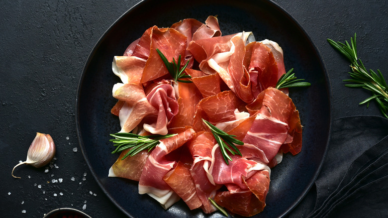 Sliced prosciutto on black plate