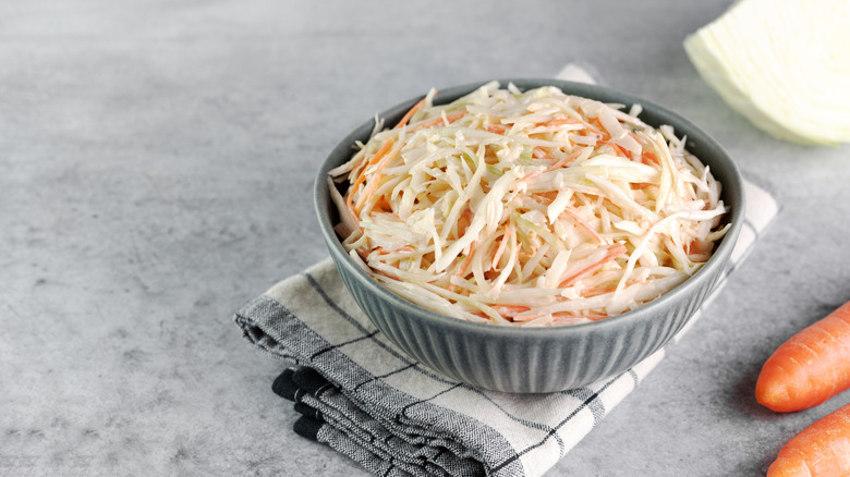 A bowl of shredded coleslaw, featuring white cabbage and carrots, sits on a folded tea towel