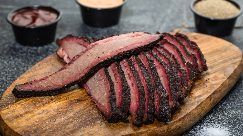 Slices of brisket on a wooden board with several sauces
