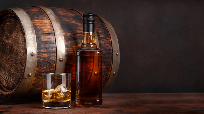 Bottle and glass of whiskey on the rocks by wood barrel