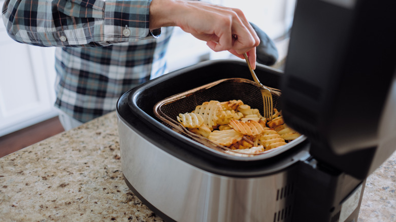 person touching fries in air fryer with fork