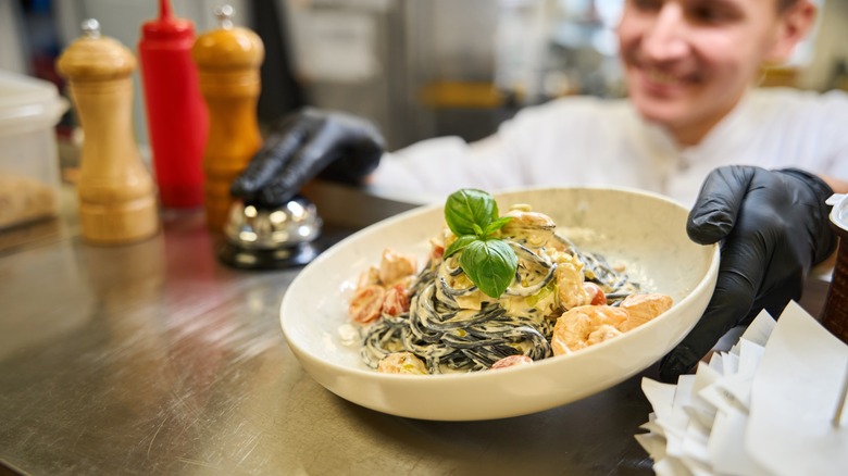 Chef holding finished dish ringing bell in pass