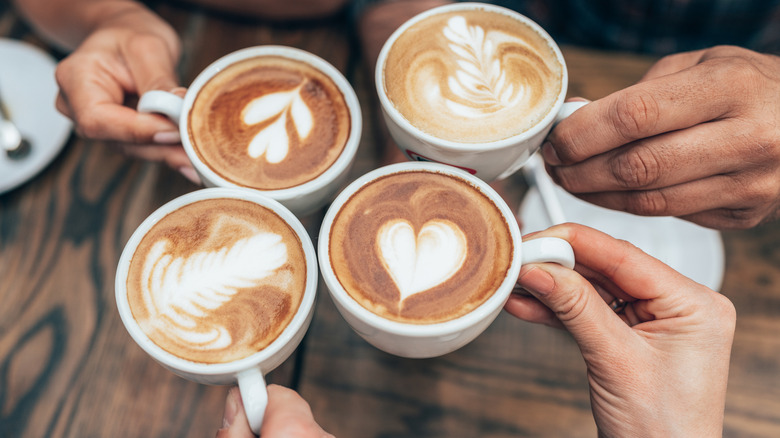 People toasting with four lattes with latte art on top