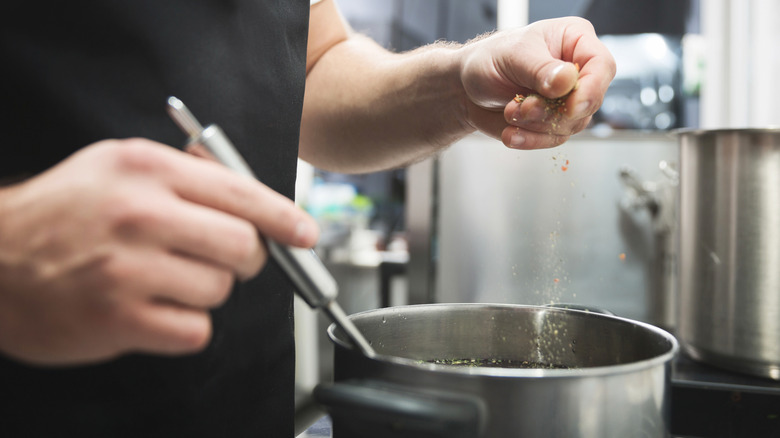 man adding spices to a soup pot
