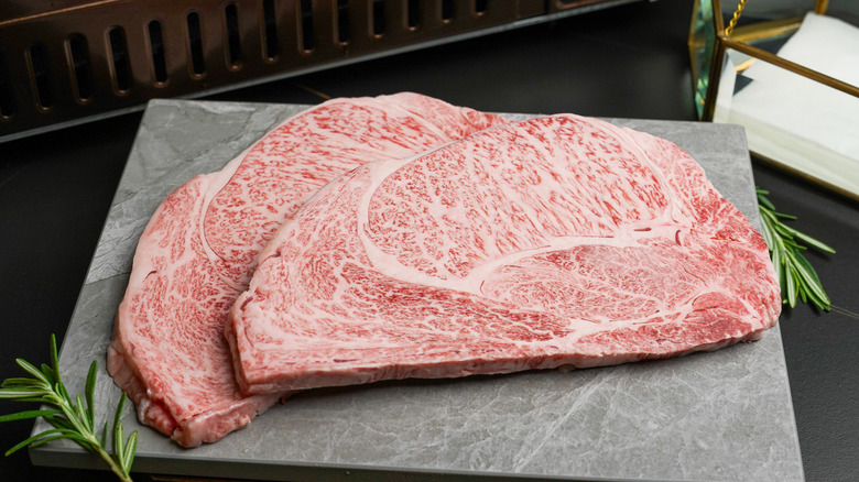 Two very marbled wagyu steaks on a slate board with single rosemary sprigs on either side