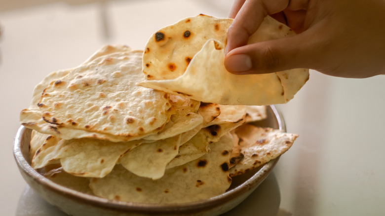 Someone picks up roti from a stack of the flat bread