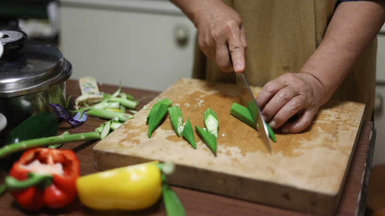 A cook slicing okra on a wooden cutting board
