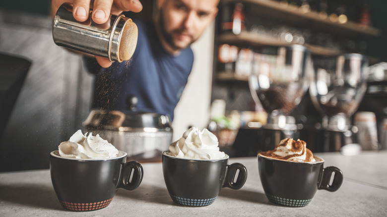 Sprinkling cocoa powder on whipped cream coffees