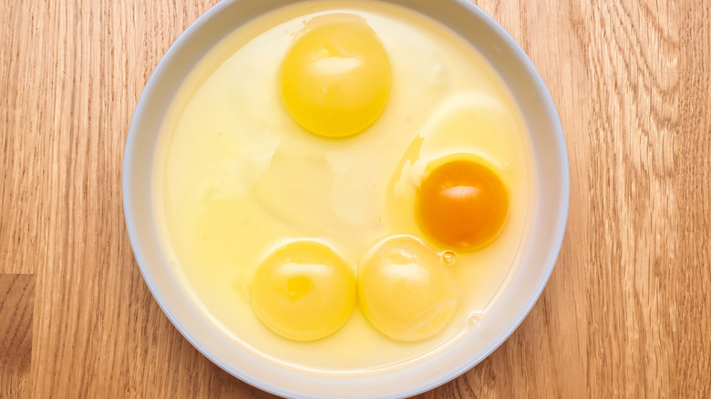 Fresh cracked eggs with different yolk colors.