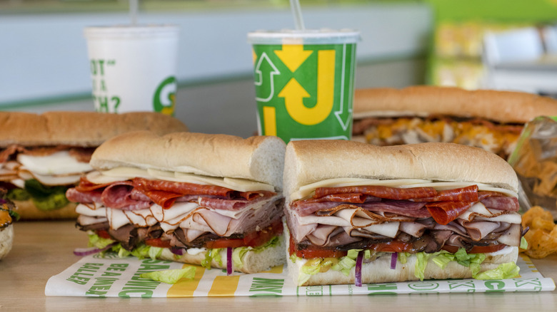 Assorted Subway drinks and sandwiches with meats, veggies, and mayo