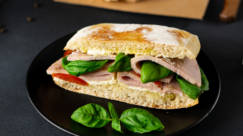 A ciabatta sandwich with ham, mayo, tomato, and fresh basil
