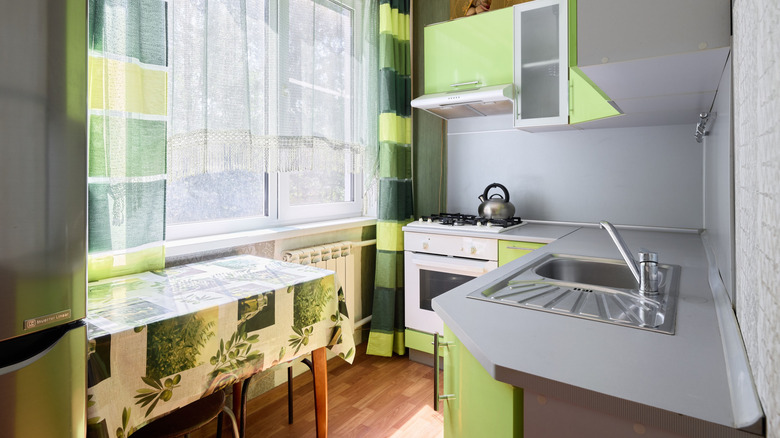 A retro kitchen with a green-patterned tablecloth and curtains and green laminate cabinets