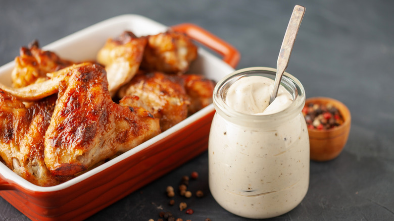 A pot of Alabama white sauce next to some freshly cooked chicken thighs.