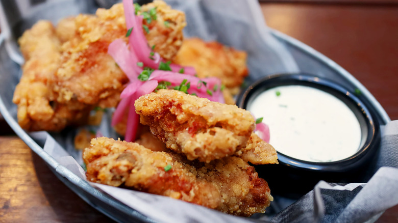 Deep fried chicken wings sit in a bowl with pickled onions next to a small pot of Alabama white sauce