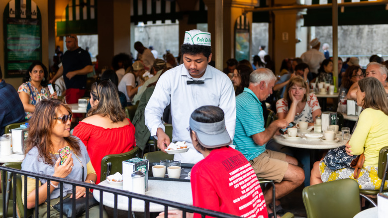 Diners at Cafe Du Monde, with a waiter serving beignets to a table