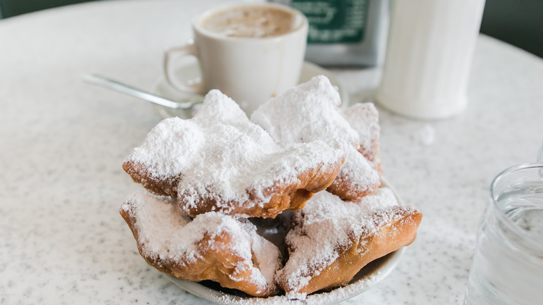 Several beignets on a plate with coffee in the background