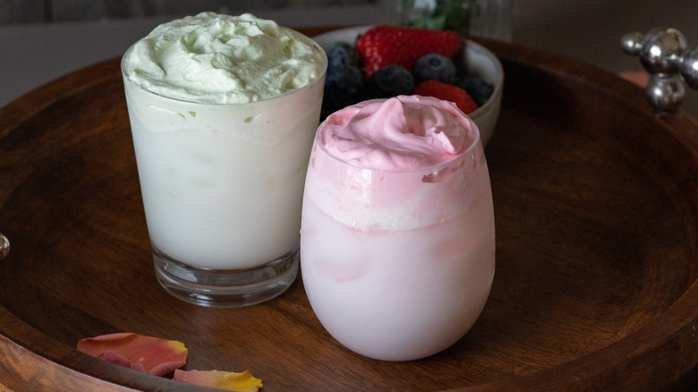 Pink and green coffees with pink and green foam on a wooden plate and berries in the background