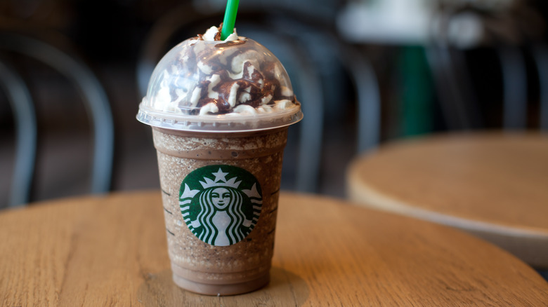 Chocolate-flavored Starbucks frappuccino with a dome lid and straw on a wooden table