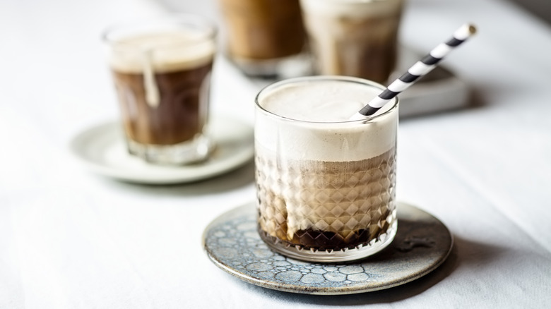 Cup of coffee with cold foam and a black and white straw on a blue saucer and white table