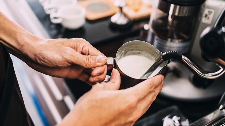 Barista using a milk frother on milk in a metal cup