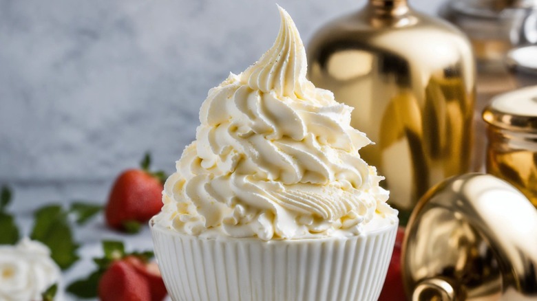 Chantilly cream in a white bowl in front of gold containers and strawberries