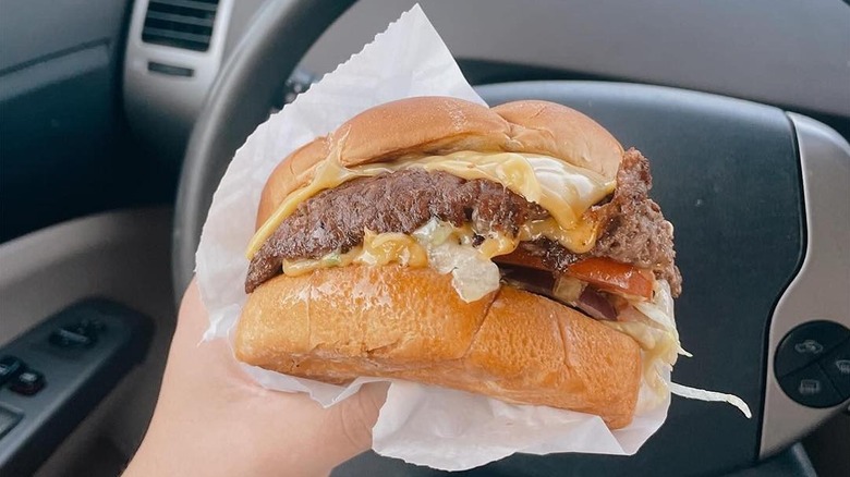 A driver of a parked car holds a Culver's Butterburger in their hand