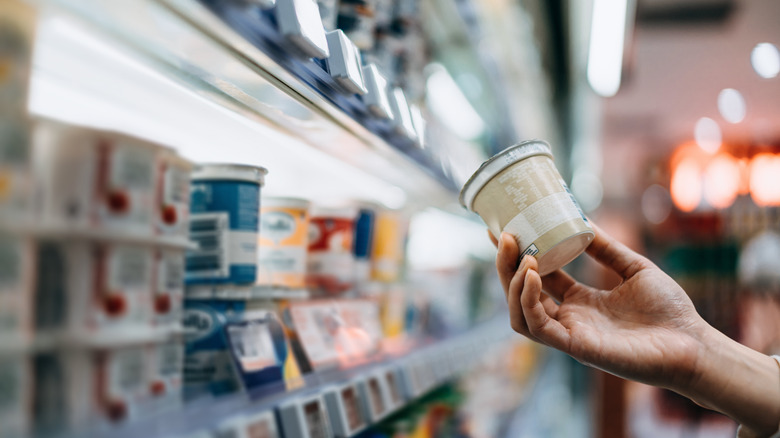 A person holding yogurt at the grocery store
