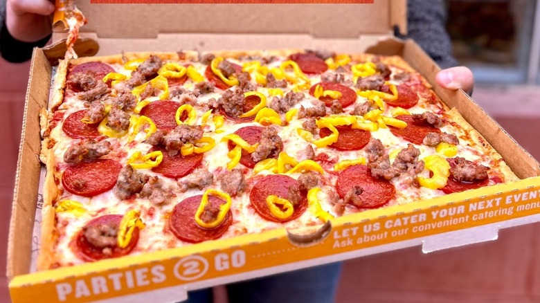 A box of Ledo's pizza topped with yellow peppers, sausage, and pepperoni.