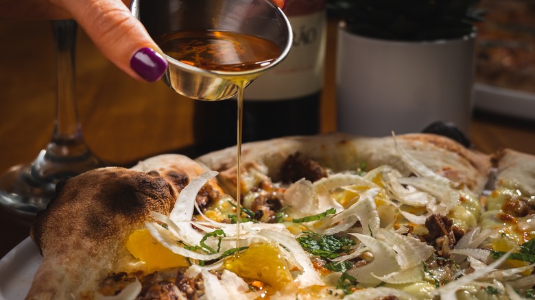 a person pouring oil over a pizza