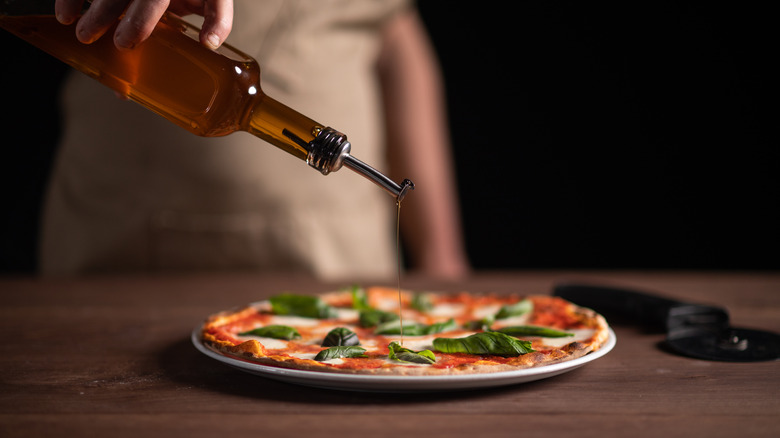 a person pouring oil over a pizza