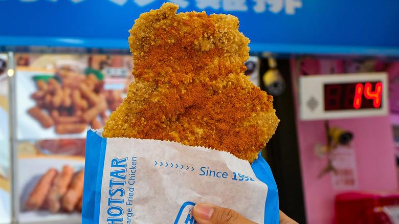 Hand holding a piece of Taiwanese XXL fried chicken wrapped in paper