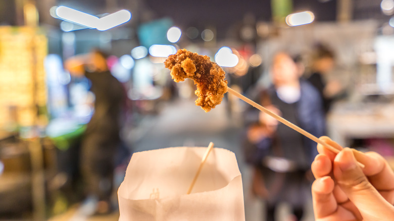 A hand holds up a skewer with a small piece of Taiwanese fried chicken at the end