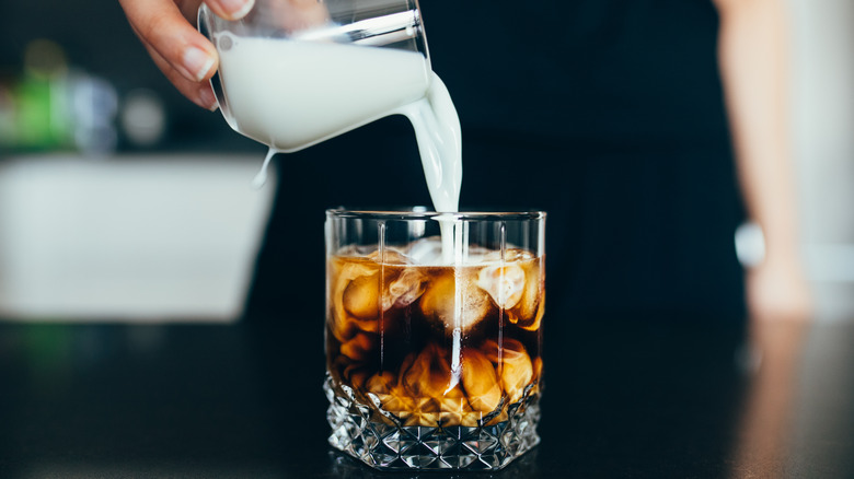 Person pouring cream into dark iced coffee
