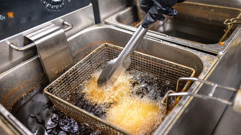 A close-up of a deep fryer with fried chicken patties grabbed with tongs.