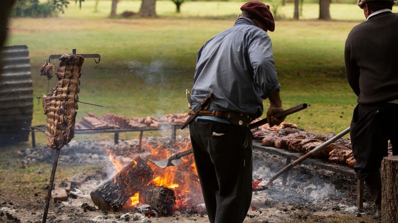 two people tending a barbecue pit with meat smoking around it