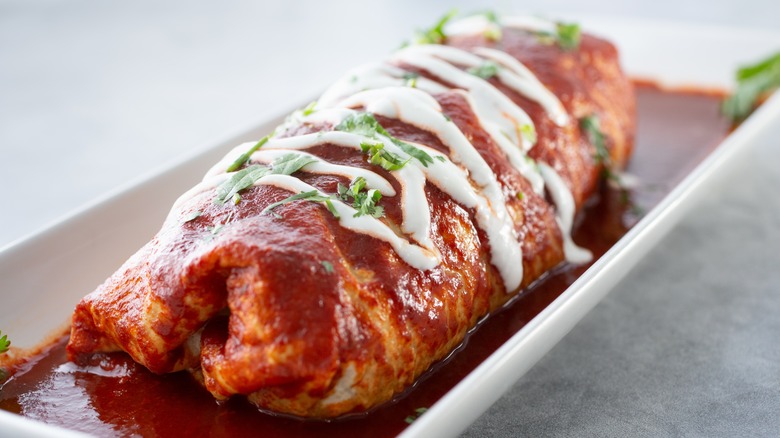 Wet burrito covered in red sauce and white sour cream