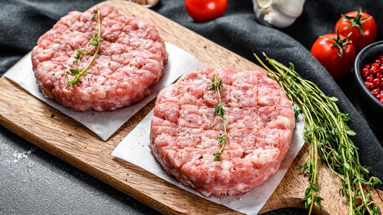 Raw poultry patties on wood block with fresh herbs