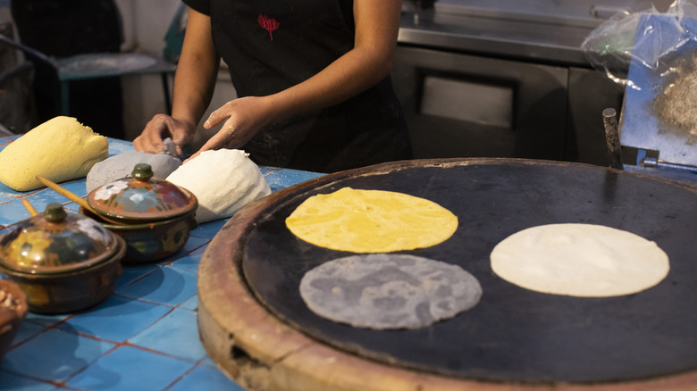 A woman makes three different kinds of tortillas on a round griddle