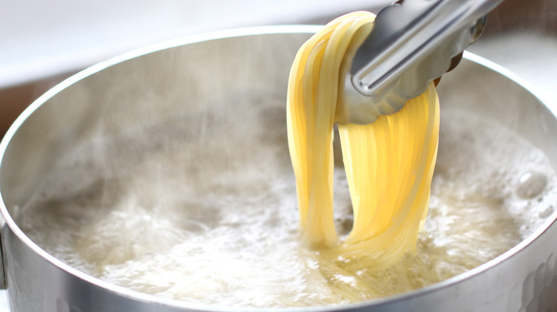 tongs removing spaghetti from boiling water