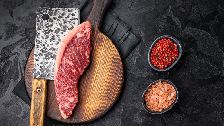 A well-marbled picanha steak next to peppercorns and salt