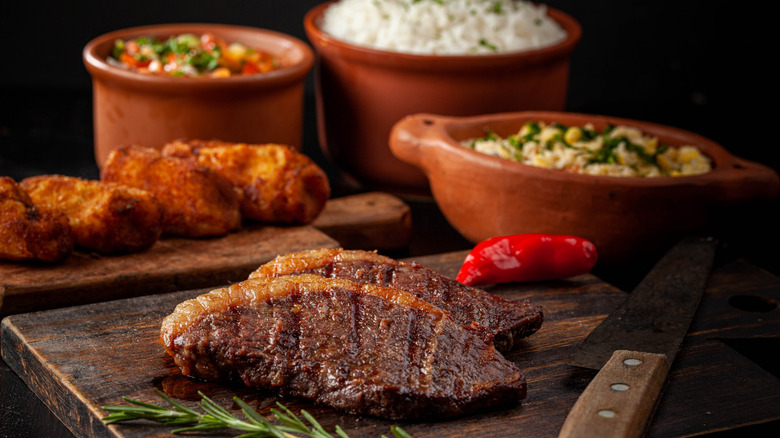 Picanha steak next to several Brazilian side dishes