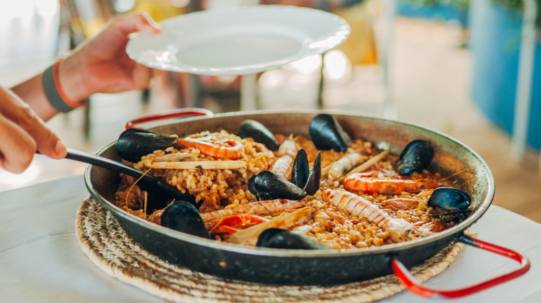 Someone scooping paella out of a paella pan onto a plate