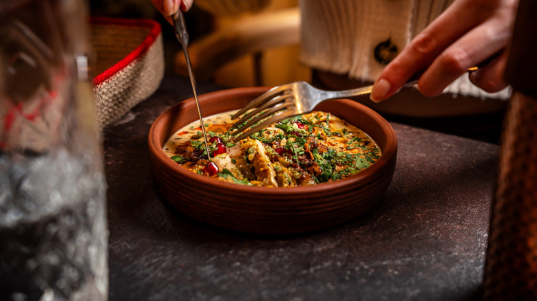 A diner is eating a rustic stew in a bowl with pomegranate seeds.