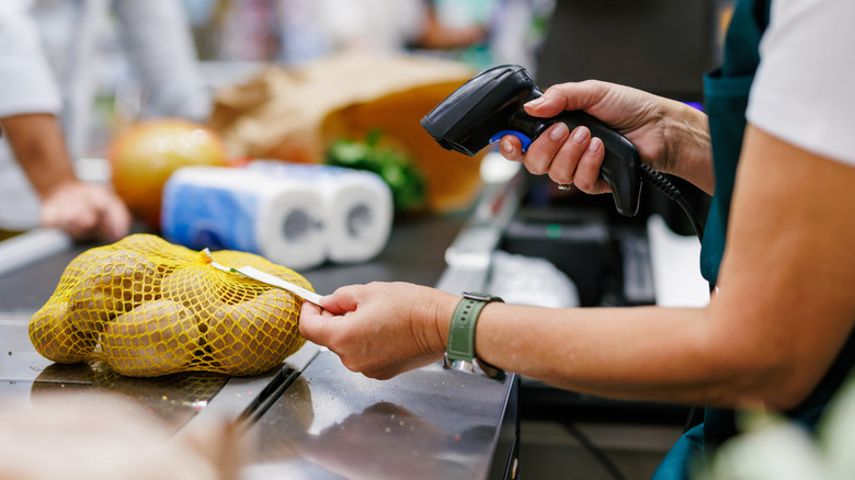 A supermarket cashier uses a handheld barcode scanner on a bag of lemons