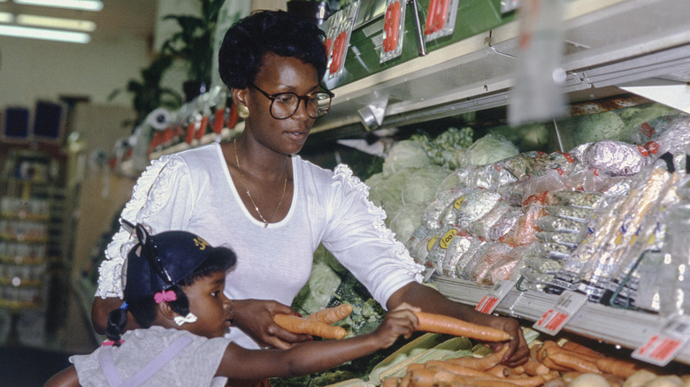 A mother and daughter shop for produce together in a 1980s grocery store