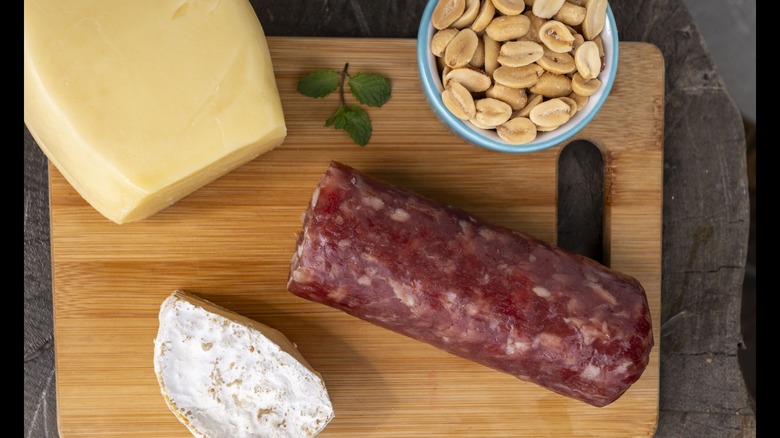 Sausage, cheese, and peanuts on a cutting board.