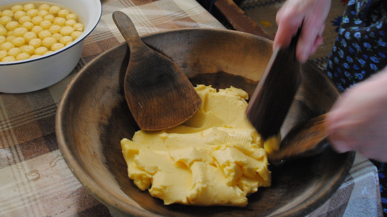 A woman holding two butter paddles gently rolls butter into a ball