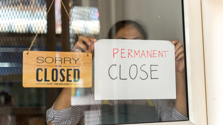 A woman puts up a sign announcing a restaurant is permanently closed